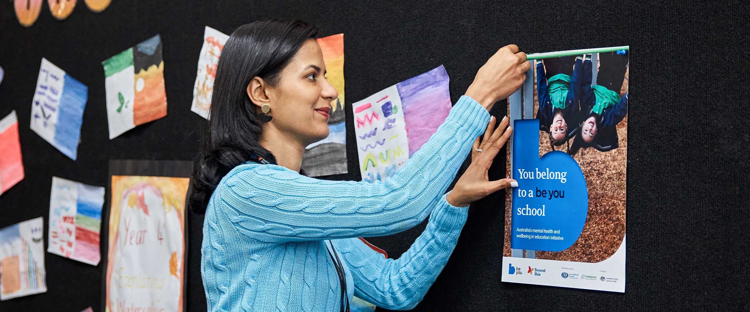 Staff examining Be You implementation tools displayed on a poster in the staffroom.