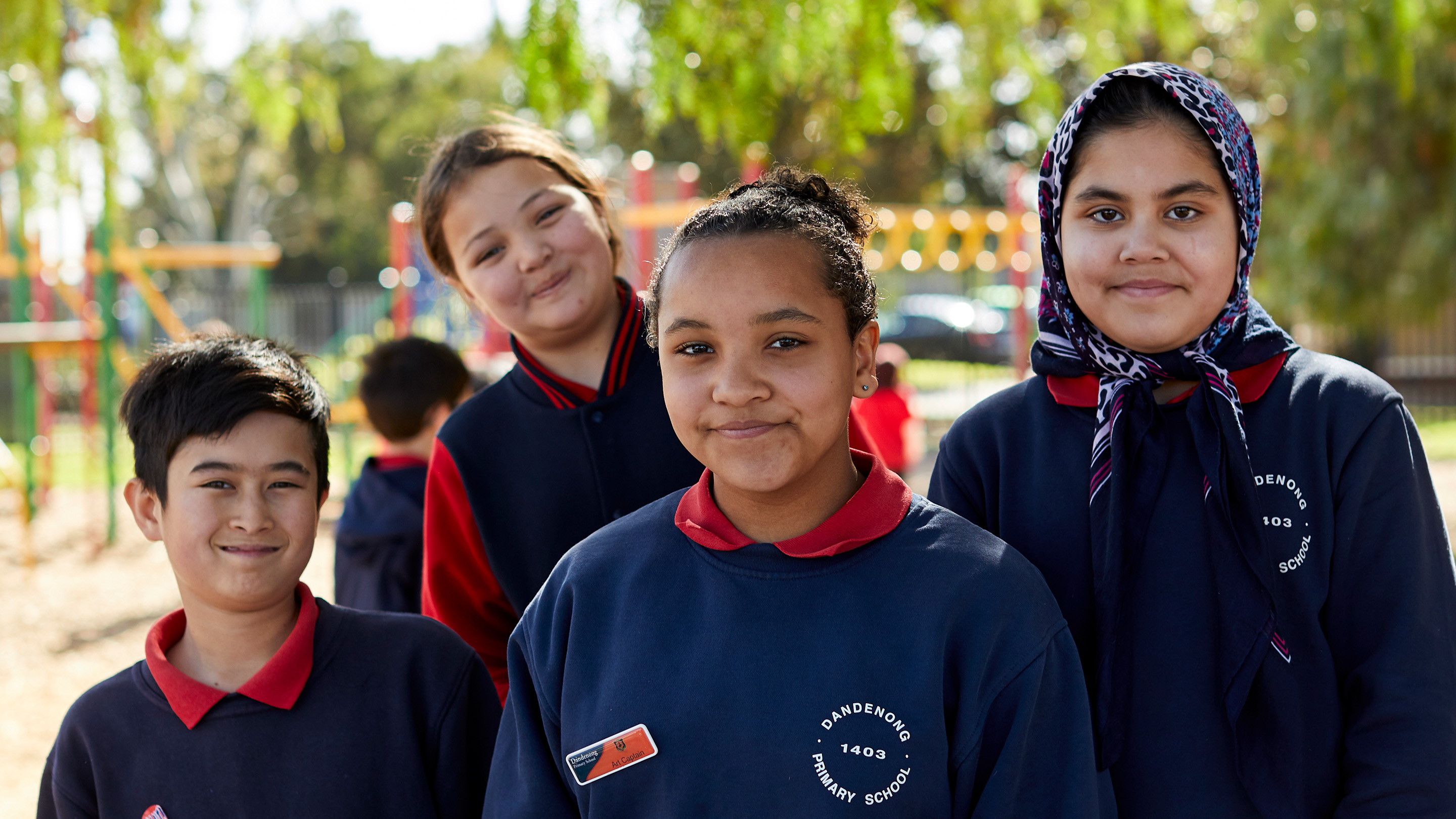 Four primary school age children standing in a playground and smiling to the camera.