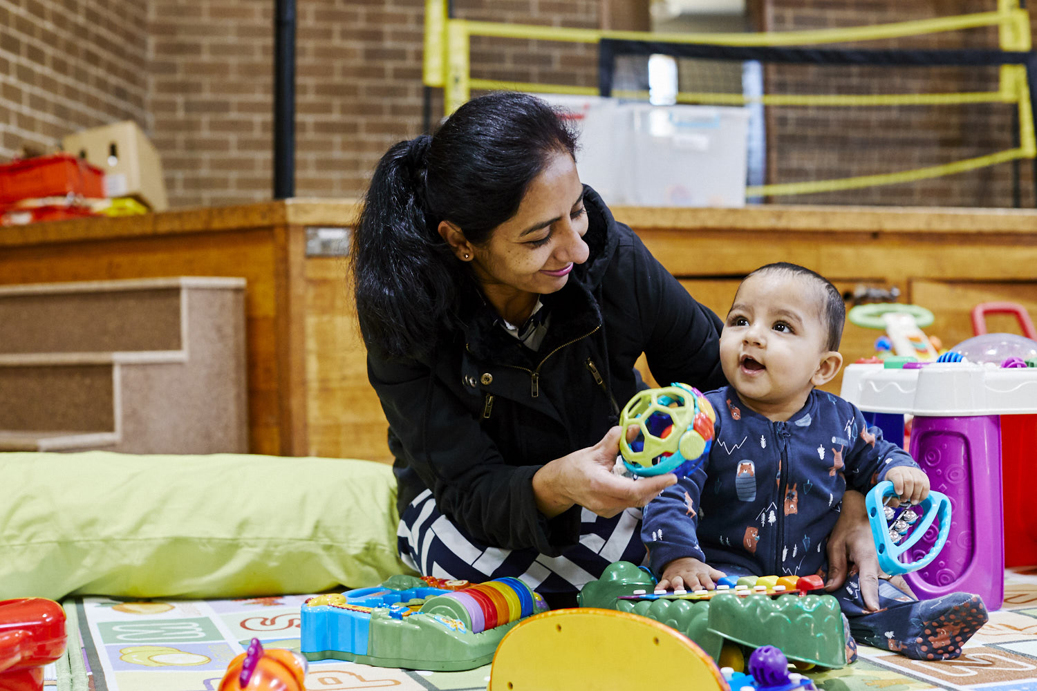 And adult and a baby sitting on the floor together, playing with toys.